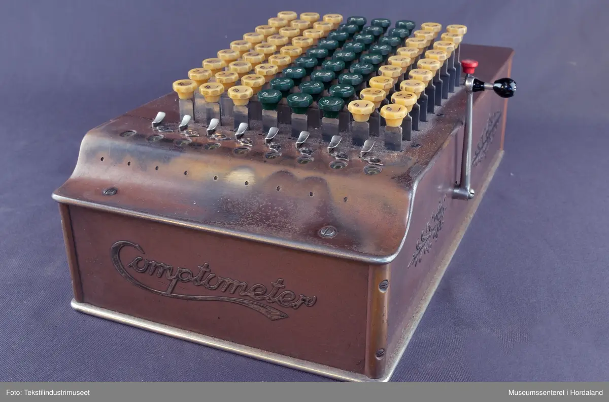 9-sifra maskin, fulltastar med gule og grøne knappar.
'Comptometer' logo på fram-og baksida. Brun med dekorasjon på sidene.