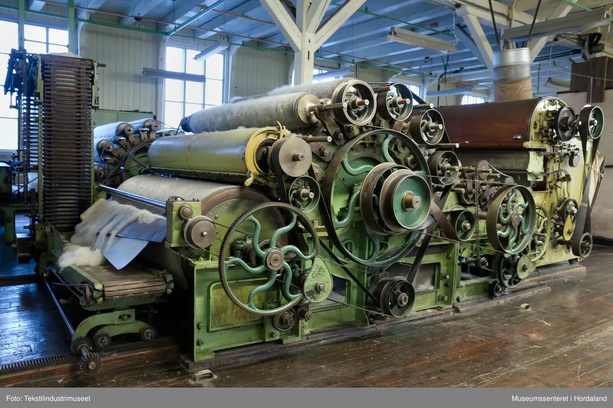 Kardeverk med tre kardemaskiner som er kopla saman og arbeider i serie, frå Oscar Schimmel & Co i Chemnitz, Tyskland. Frå ullinntaket i eine enden av maskina, blir ulla ført over valsar med metallkardar på, som fjernar ureinheiter og løyser opp floker i ullfibra. Ulla blir karda ein gong før den går over eit transportband i tre, blir snudd og karda to gonger til før det karda ullfloret går gjennom ein flordelar som deler det opp i remser. Remsene blir rulla opp på store metallspolar, og blir då kalla forgarn. I forgarnet ligg alle ullfibra etter kvarandre, men garnet er utan styrke og må spinnast for å bli til brukbart garn. 

Maskina var i bruk på Salhus Tricotagefabrik (1859-1989), og hadde her internt maskinnummer 5. Kardeverket står i hesteskoform med ullinntaket og ei kardemaskin på ei sida, to kardemaskiner og flordelaren på andre sida, og eit transportband i tre som bindeledd mellom dei to. Kardeverket blir drive av tre elektriske motorar som er festa til golvet på innsida av 'hesteskoen'. Maskina er grønmåla, med mange dekorative tannhjul med bua eiker, typisk for maskiner frå rundt 1900.

Det har seinare blitt montert ein støvsugar på kardeverket, som syg opp støv ved flordelaren, og transporterer det tilbake til ullinntaket. Røyra til støvsugaren ser 'heimelaga' ut, og er sett saman med bl.a. teip og ulike typar røyr.