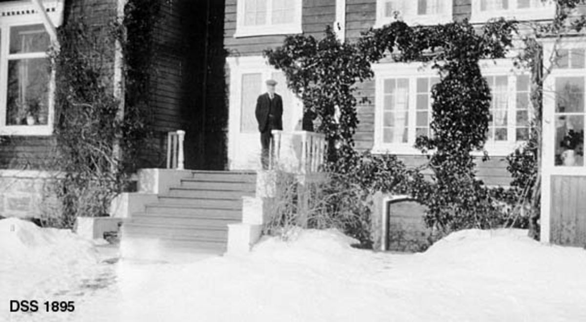 Skogforvalter Jakob Gylding Preuthuns villa i Molde.  Fotografiet er tatt mot midtpartiet av den toetasjes bygningen (jfr. DSS 1894).  Her er det ei bred trapp hvor skogforvalteren står foran ei tobladet inngangsdør.  Bygningen har horisontal veggpanel som er malt i mørk farge, mens dør- og vindusomramminger samt hjørnekasser er kvite. Bygningen er reist på en gråsteinsmur.  En del klatreplanter vokser oppetter veggene.  Hagen i forgrunnen er snødekt. 