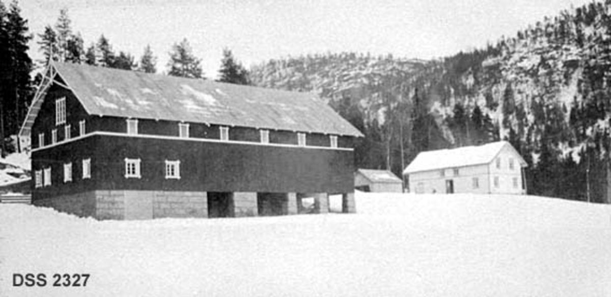 Garden nordre Henseid i Drangedal.  Vinterbilde med snødekt åker i forgrunnen gardstunet med driftsbygning (jfr. DSS 2326), våningshus og garasjeliknende skur i mellomgrunnen og berg med spredt barskog i bakgrunnen. 