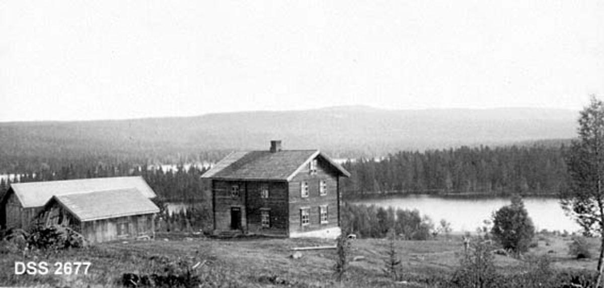 Bebyggelsen på garden Voie i Gran bygdeallmenning.  Laftet våningshus, vedskjul som delvis skjuler driftsbygningen.  Bakenforliggende vatn (Skiten) og skogvidder. 