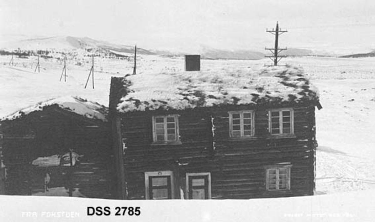 Fra Fokstua fjellstue på Dovrefjell.  Den gamle bubygningen og våningshuset "Søpå", fotografert før bua ble flyttet på 1920-tallet.  Lyslinje og snødekt fjellandskap i bakgrunnen. 