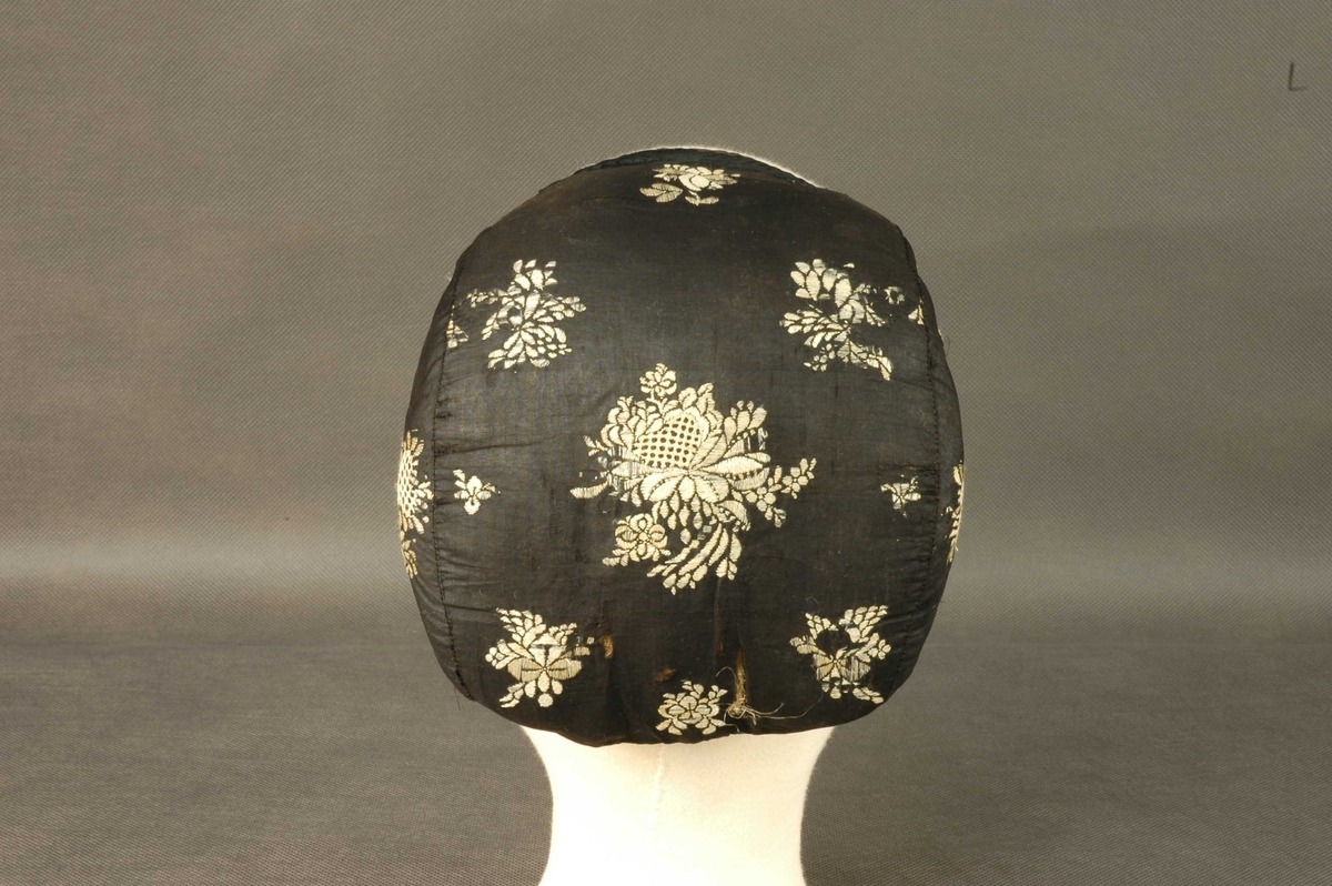 Ørelue i svart silke med hvite broderte roser. Ingen dusk. Foret med lyst linstoff. Svarte knytteband.