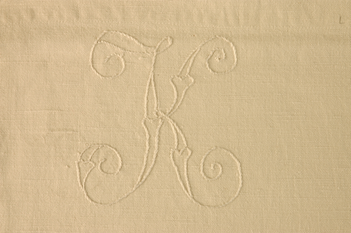 Hvitt laken med påbrodert initial "K".