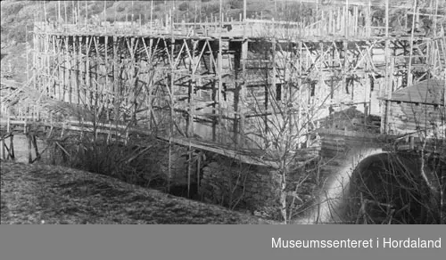 Herlandsfossen Kraftstasjon under oppføringa, elva renn på utsida, stort vannhjul plassert ved anleggsbrakke