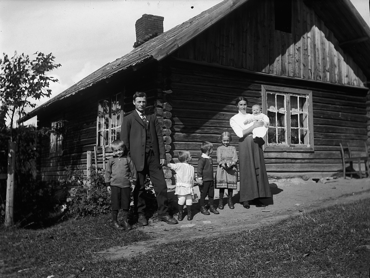 Familie utenfor tømmerstue. Karl Slåtten og kona Birgitte. Helskjær, Helgøya. 