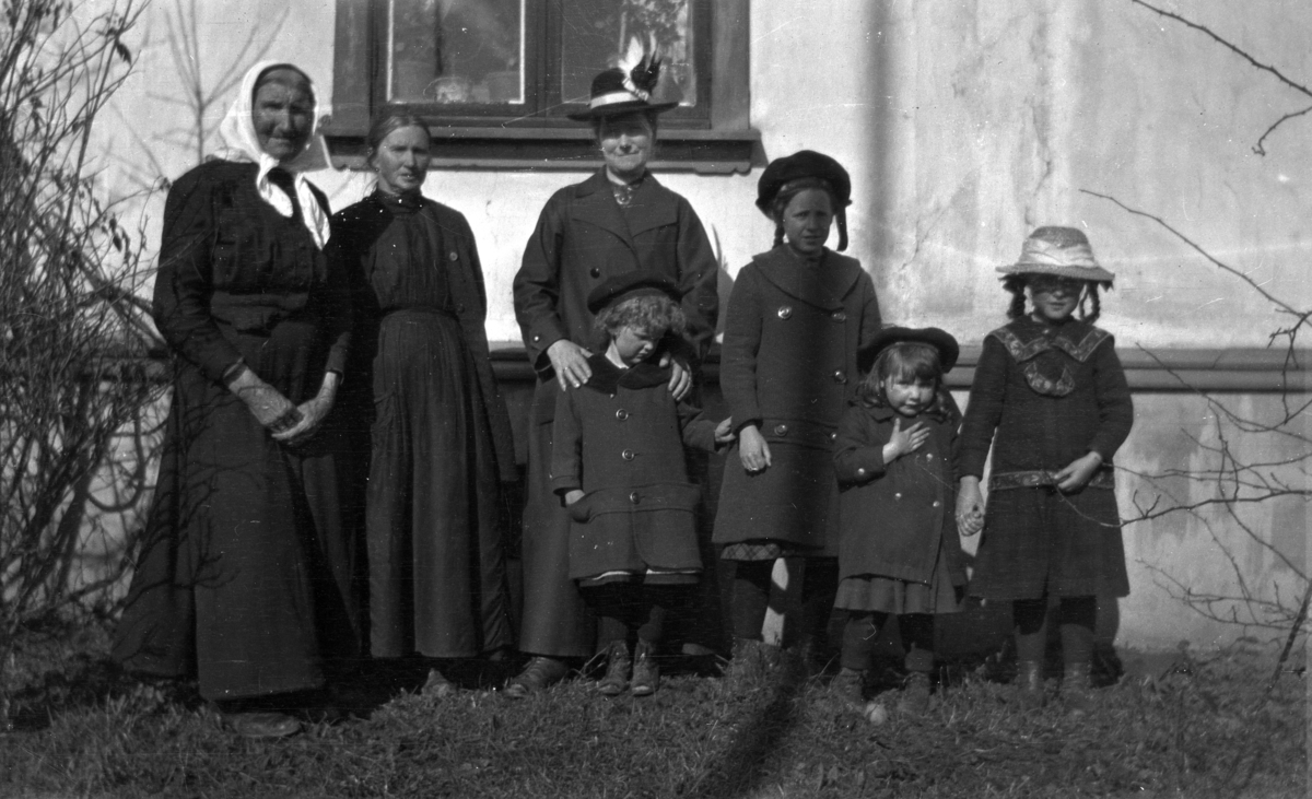 Gruppe ukjente kvinner og barn foran et hus. 