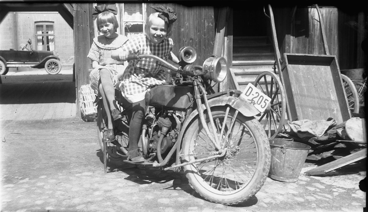 Hamar, Strandgata 15, baker og konditori O. Johannessen (Bager & Conditor), etablert i1902, drift fram til 1958, sønnen bakermester Johs. Johannessen tok over etter faren Olaus Johannessen i 1916, motorsykkel med registreringsnummer D-205 i bakgården,
To unge jenter på en Indian Scout 600 cc fra 1925-1926.