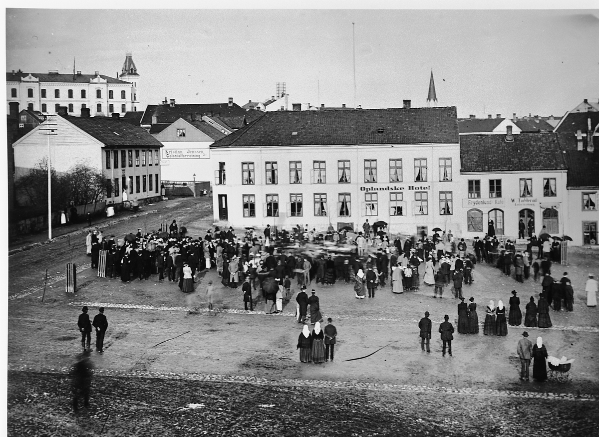 Hamar, Stortorget, Torggata 82. veggreklame: Kristian Jenssen Colonilaforretning, Oplandske Hotell. Frydenlunds kafe, garvermester Wictor Toddeud, arrangement på torget med mye folk i pene klær,