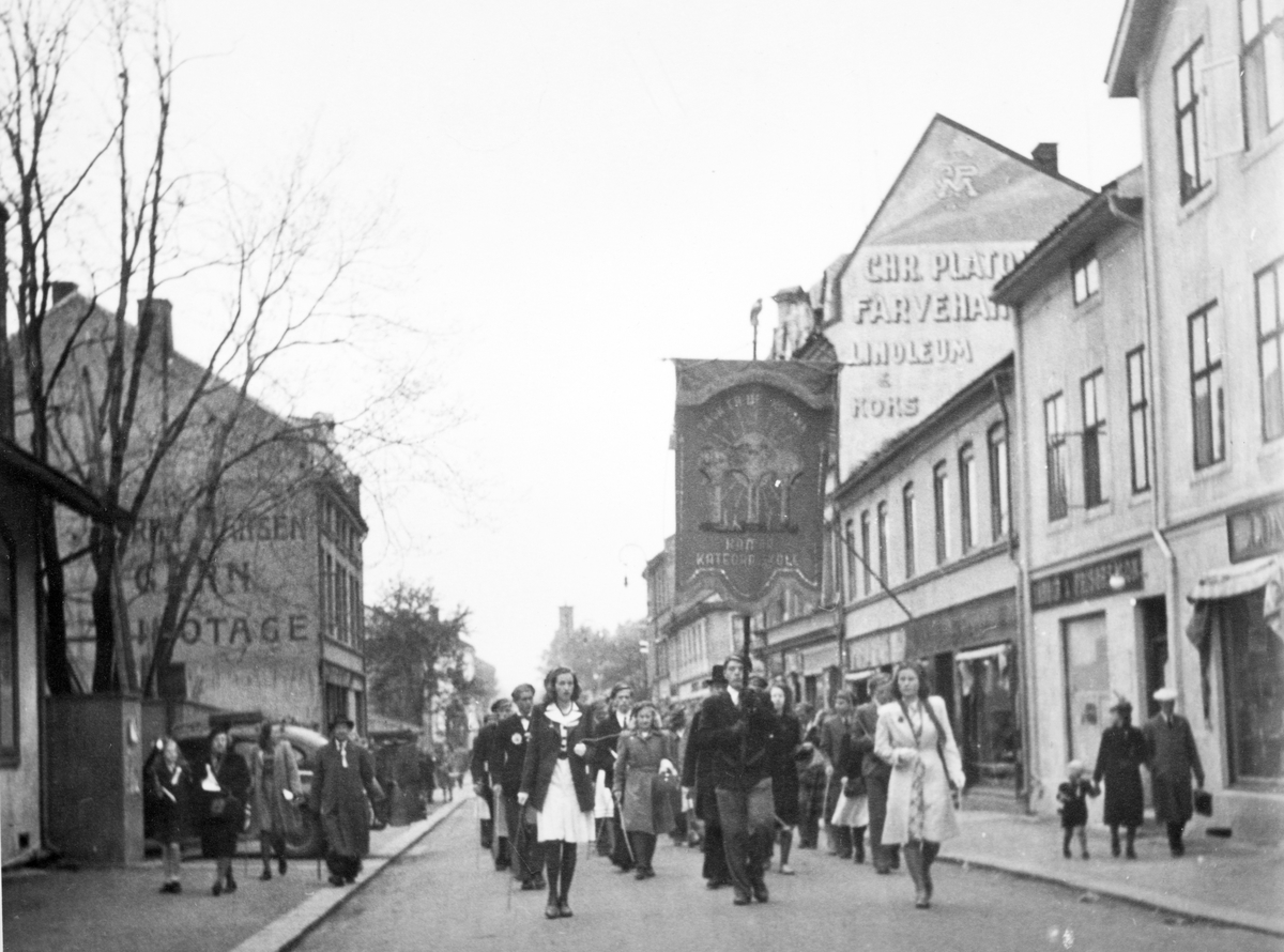 Skoletoget passerrer gjennom Torggata 17. mai 1945. Fredsdagene etter 2. verdenskrig. Elever, russ fra Hamar katedralskole. Skolefane. 