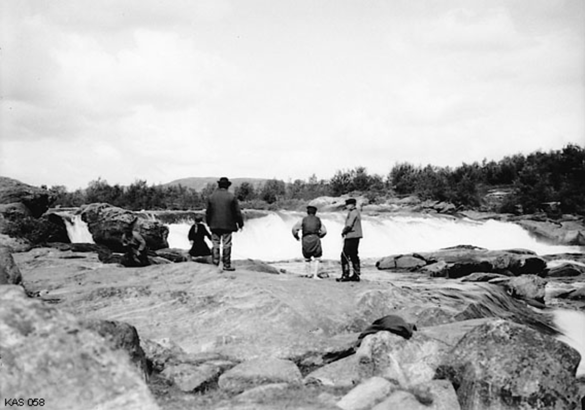 Fra det såkalte «käpäläfisket» i Skoltefossen i Neidenelva i Finnmark i 1912.  Fotografiet er tatt fra en posisjon like nedenfor fossefallet.  Vi ser et kastelag på fem karer.  Tre av dem skulle kaste den fem meter lange nota slik at den bredte seg som ei vifte over kulpen under fossen, der laksen sto.  To andre karer, som sto på et steinskjær nedenfor (til høyre på dette fotografiet) holdt i tau som var knyttet til endene av notveven.  Så snart undertelna på nota nådde botnen begynte karene å trekke den mot land på et sted der det var en god landingsplass for laksefangsten.  Det ble oftest tatt flere lakser i hvert kast.