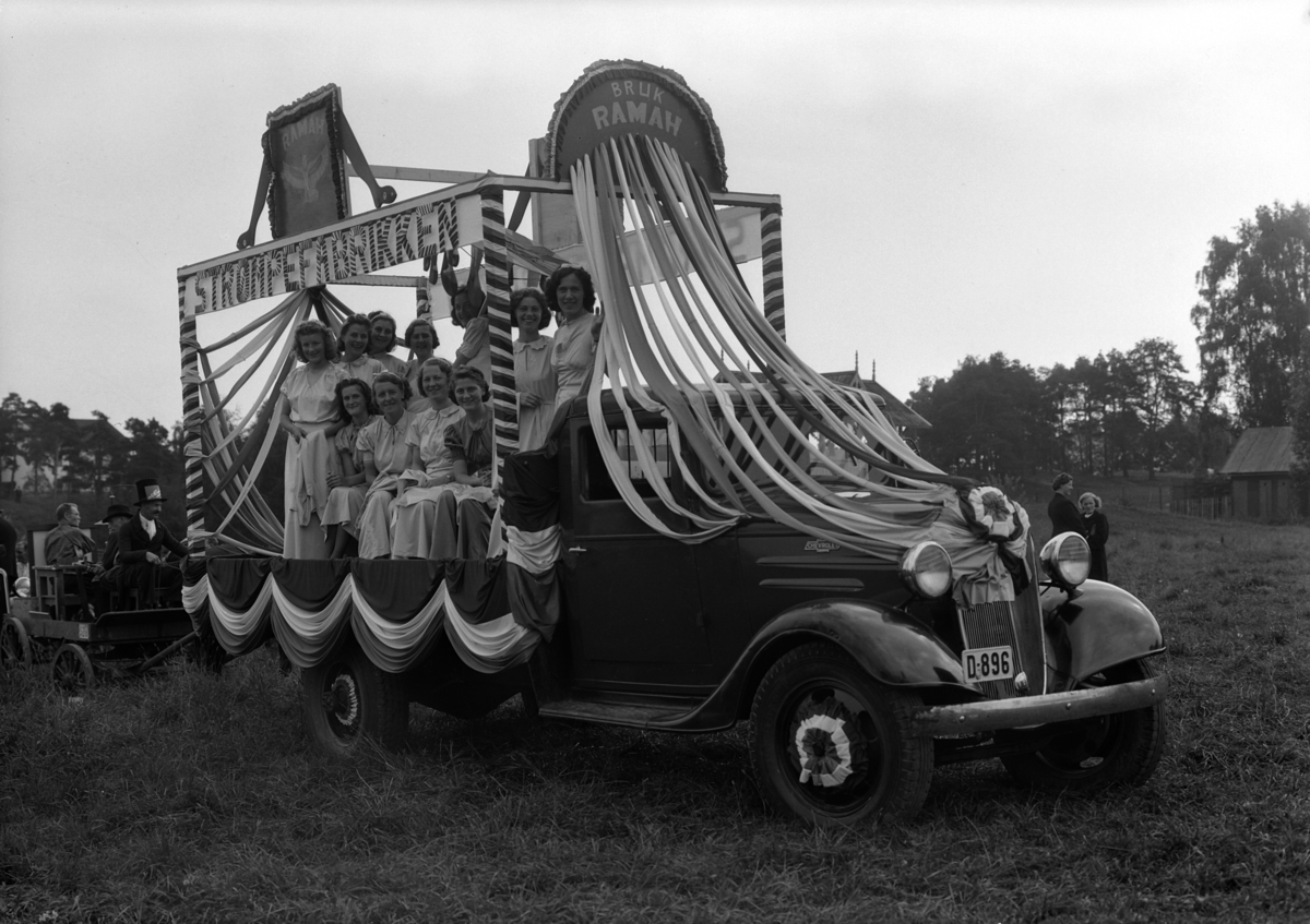 Hamar, Hamardagen 1939, lastebil med reklame for strømpefabrikken RAMAH pyntet med blomster, dagen var en todagers fest som samlet 50 000 mennesker, bilkortesje som representerte distriktets handel, håndverk og industri, vognmann Aage Larsen sin lastebil Chevrolet 1936 modell med registreringsnummer D-896, "syerskene" på lasteplanet foran fra venstre: Frida Olsen, Benny Paulsen, Laila Morbech, Åse Larsen, bak fra venstre: Signe Rosenborg, Bodil Hernes, Elsa Sæther, Kristine Korslund, Ruth Kjendsli, Agnes Løvmo og Marta Larsen,