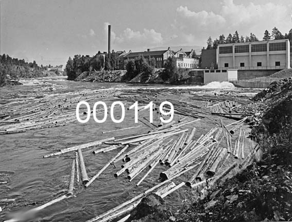 Drammenselvens Papirfabrikker (Union Geithus) i Modum i Buskerud.  Fotografiet er tatt etter at den nye kraftstasjonen, «Geithusfoss II», var ferdig, altså etter høsten 1961.  Fotografen har stått i en elvesving nedenfor bedriften og vendt kameraet oppover.  I forgrunnen ses elva med en del barket fløtingstømmer.  Bakenfor ses Geithusfossen til venstre.  Sentralt i bildets øvre del ligger papirfabrikken med «Nysalen» fra 1912 i forgrunnen.  Til høyre for denne igjen ses den nye kraftstasjonen i funkisstil.  Stasjonen ble for øvrig bygd av Thor Furuholmens entreprenørselskap.