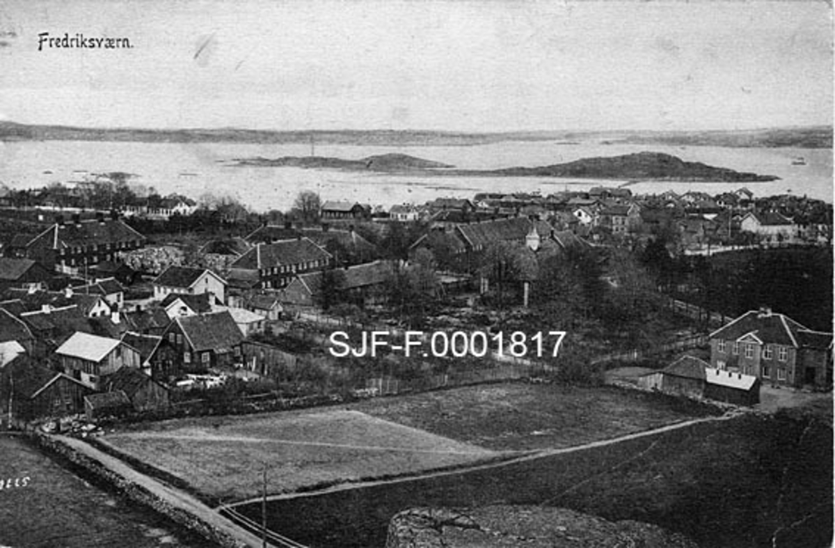 Fredriksvern, orlogsbasen i Stavern i Vestfold.  Den dansk-norske kongen Fredrik V etablerte galeiverft og flåtestasjon her midt på 1700-tallet.  Beliggenheten var gunstig, med ei havn som lett lot seg beskytte, og med overkommelig avstand både til tvillingriket Danmark og det fiendtlige Sverige.  Etter Kiel-freden og tumultene i 1814 ble Fredriksvern utdanningssted for norske sjøoffiserer.  Midt på 1800-tallet ble denne virksomheten flyttet til Horten, mens Fredriksvern ble øvingssted for Krigsskolen.  Anlegget var under tysk kommando under 2. verdenskrig og ble blant annet brukt til internering av russiske krigsfanger, norske studenter og lærere.  Etter krigen har Luftforsvaret brukt anlegget.  Fotografiet er tatt fra en bergnabb ned mot de militære anleggene med omliggende sivil bebyggelse, og med Larviksfjorden og noen av dens øyer i bakgrunnen. 