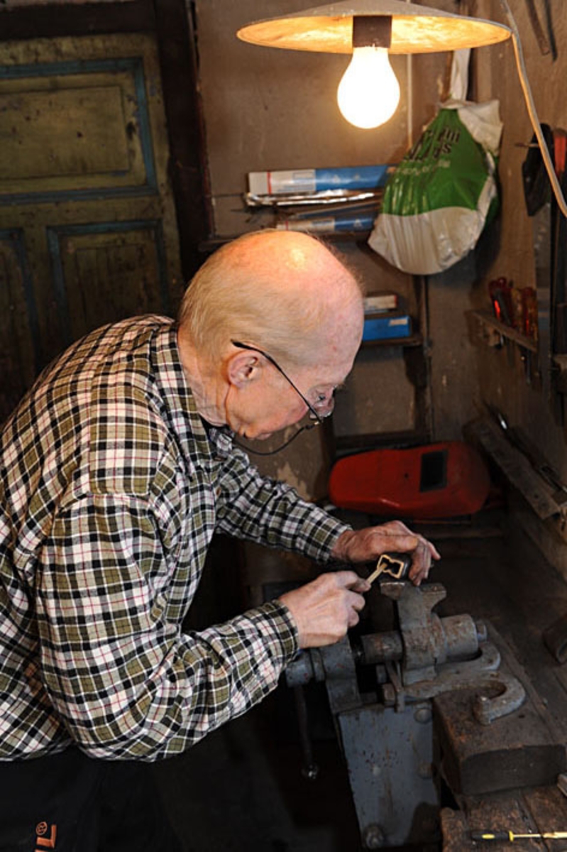 Smeden Oddbjørn Knudsen (f. 1935) filer det profilerte eggpartiet på ei nysmidd merkeøks.  Fotografiet er tatt i verkstedrommet i Knudsen-smia i Mjøndalen (Nedre Eiker kommune), der Oddbjørn er tredje generasjon i en smedfamilie som spesialiserte seg på leveranser av merkeøkser til tømmermålerne langs norske fløtingsvassdrag.  Smeden har festet økseholdet i ei skrustikke på ytterkanten av en arbeidsbenk.  Han filer innsida av den profilerte eggen.  Poenget var at eggen her måtte være rett, slik at øksa ”beit med seg” fliser av yteveden på tømmeret når merkerne hogg i stokkene.  