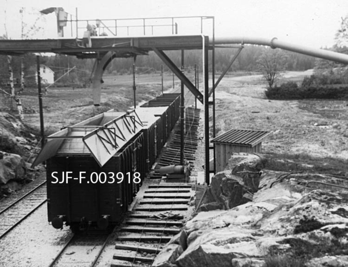 Lastestasjon for celluloseflis ved Geithus Bruk på Modum i Buskerud.  Fotografiet er tatt i 1967, da produksjonen ved denne bedriften startet. Etter at tømmeret var kappet til kubb, barket og hogd til flis, ble sluttproduktet kastet over i en silo.  Derfra ble den transportert ned i en slusemater hvor flisa ble tatt av en luftstrøm som med en hastighet av 40 meter i sekundet blåste den mot lastestasjonen for jernbanevogner, som vi ser på dette fotografiet.  Her munnet flisrøret i et pendelrør som kunne beveges i vognenes bredde- og lengderetning, slik at flisa ble jevnt fordelt. Lastinga ble for øvrig fjernstyrt fra sorteringsavdelingen inne i fabrikkhallen, hvor det var monitorer som gjorde det mulig å følge oppfyllinga av vognene.  NSB leverte spesialvogner med høye karmer for denne transporten.  Hver vogn kunne ta 66 kubikkmeter flis.  Geithus Bruk skulle kunne fylle 15 fulle vogner hver dag.  Laste- og losseanlegget skal ha vært det første i sitt slag i Europa.  Flisa gikk stort sett til Skotselv Cellulosefabrikk i Øvre Eiker. 