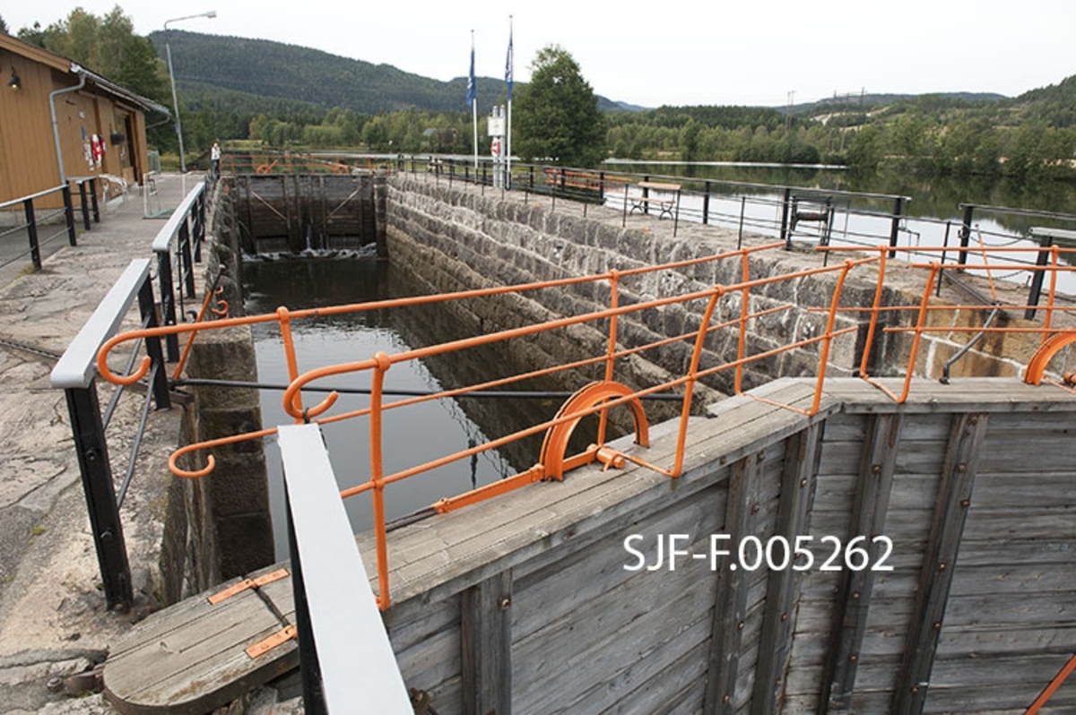 Slusekammeret i Lunde sluse i Bandak-Norsjø-kanalen i Telemark.  Fotografiet er tatt fra slusekammerets sørøstre hjørne.  Slusekamrene i denne kanalen er bygd for å skape passasje for fartøyer som var inntil 31, 4 meter lange, 6, 6 meter brede og stakk inntil 2, 5 meter djupt.  De var omgitt av fugete murer av hoggen naturstein, og hadde porter av tre med smijernbeslag.  Botnlukene ble åpnet ved hjelp av spaker oppå portene, og når portene skal åpnes brukes spett i perforerte skinner på murkronene.  I 1970- og 80-åra argumenterte Skiensvassdragets fellesfløtningsforening, som var den største brukeren av kanalen, for at slusene måtte få glatte vegger og porter med motoriserte åpne- og lukkemekanismer.  Dette kravet ble innfridd ved Skien og Løveid sluser, men aldri i Bandak-Norsjø-kanalen, som ble drevet videre som «museumskanal». 