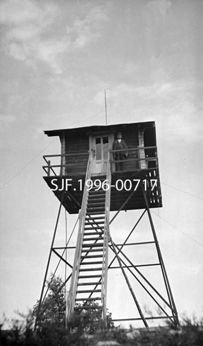 Tårnet på Kjerringa skogbrannvaktstasjon 213 meter over havet på grensa mellom Tune og Svinndal i Østfold.  Fotografiet skal være tatt i juni 1921.  Firmaet And. H. Kiær & Co. Ltd., som eide både skog, sagbruk og treforedlingsindustri, skal ha bekostet bygginga av dette anlegget, med supplerende bidrag fra en del skogeiere i Østfold.  Smaalenenes skogselskap og forsikringsselskapet Skogbrand skal seinere ha samarbeidet om vedlikehold og drift av dette anlegget. 

Understellet på tårnet består av jernskinner.  Fire hjørneskinner skrår innover mot tårnets sentralakse og er avstivet med horisontale som diagonale (krysslagte) komponenter.  På toppen av jernkomponentene - anslagsvis fire-fem meter over bakken - er det en platting hvor det er reist ei lita laftehytte med saltak.  Atkomst til hytta skjer via trapp fra bakken opp mot ei dør på ei av hyttas langsider.  I gavlen er det et forholdsvis bredt vindu. Ei stang som stikker opp om lag midt på taket tjente antakelig som lynavleder.  Rundt hytta er det en "balkong" med et smalt gangareal avgrenset av et jernrekkverk.  Fotografiet er tatt fra bakken mot fronten av brannvakttårnet med trappa opp til hytta i forgrunnen.