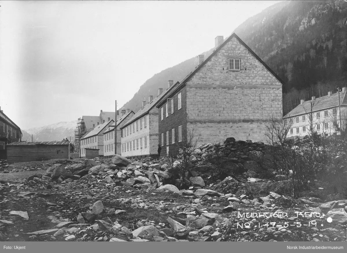 Fire murhus i Tveito Alle på nordsiden av veien bygges. Lager stående midt i gaten. I bakgrunnen bygges Tveito skole. På nordsiden av murhusene sees murbebyggelsen i Sam Eydes gate.