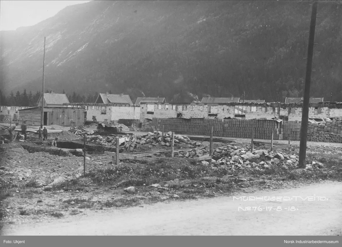 Murbebyggelse i Tveito Alle under bygging. Bolighusene på sørsiden av gaten er bygget opp til første etasje. Byggene på nordsiden av gate graves det ut kjellere til. Boligbebyggelsen av typen Egne hjem i bakgrunnen.