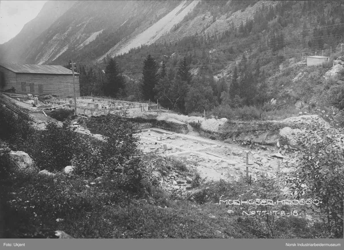Murhusbebyggelsen på Krosso under oppføring. Grunnarbeid for to murhus er påbegynt. Bygg i tre øst for grunnarbeidene. Bygninger på sørsiden av juvet langs Vemorksporet.