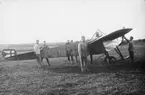 Flygplan M 1 Nieuport IV G på Axevalla hed, 1912. Flygförare i förarsits och sex personer ståendes runt flygplanet.