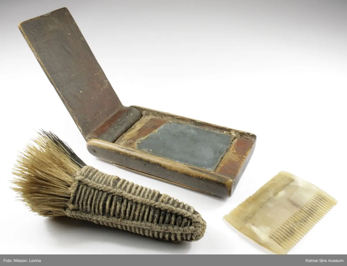 KLM 9855:1-2. Rakdon, består av borste och etui med spegel och luskam. :1 borste, längd 12 cm, diameter som mest 5 cm. :2 etui med spegel och kam, längd 11,5 cm, bredd 6,2 cm, tjocklek 1,8 cm. Borste av svinhår. Etuiets ena sida kan öppnas helt och har en spegel på insidan. Etuiets andra sidan har ett fack med skjutlock, i facket ligger en kam av ben. Dubbelkam, ena sidan kan användas som luskam.