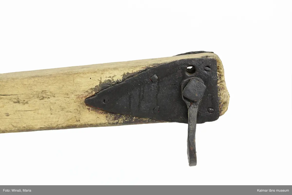 KLM 12823. Plog, trä, metall. Plog med handtag och ås av trä. På åsens ena sida sitter en rist av järn fastskruvad. Längst ut på åsen en dragkrok av järn för anspänning av dragdjur. Plogblad med bill av järn. Träkil mellan plogblad och landsida. Plogen är järnskodd på undersidan. Den har även varit järnskodd på landsidan men denna saknas. Spikarna sitter kvar i träet. Fyra slåar mellan handtagen, två av järn och två av trä. Det nedersta är fastskruvat i plogbladet. Plogen är svartmålad med en röd eventuell rostskyddsfärg under. Målad under senare tid.