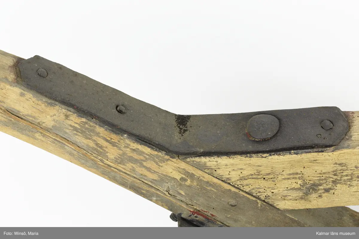 KLM 12823. Plog, trä, metall. Plog med handtag och ås av trä. På åsens ena sida sitter en rist av järn fastskruvad. Längst ut på åsen en dragkrok av järn för anspänning av dragdjur. Plogblad med bill av järn. Träkil mellan plogblad och landsida. Plogen är järnskodd på undersidan. Den har även varit järnskodd på landsidan men denna saknas. Spikarna sitter kvar i träet. Fyra slåar mellan handtagen, två av järn och två av trä. Det nedersta är fastskruvat i plogbladet. Plogen är svartmålad med en röd eventuell rostskyddsfärg under. Målad under senare tid.