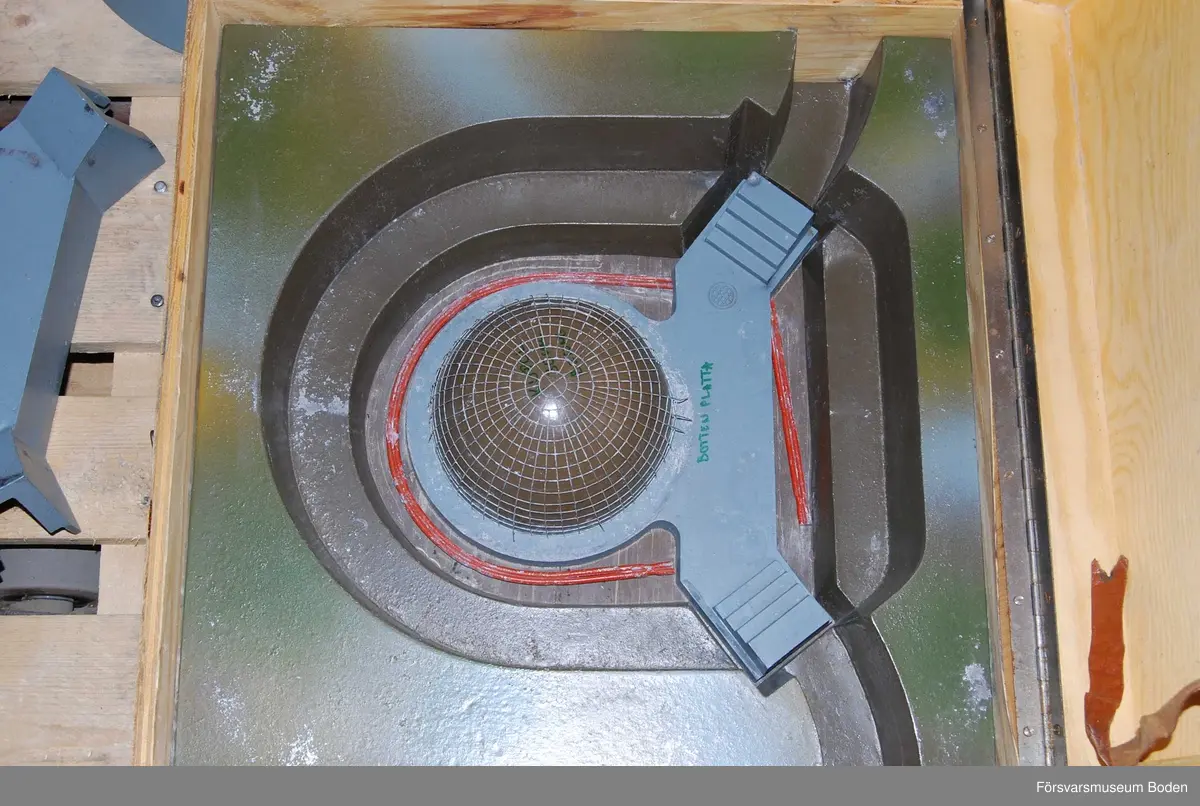 Modell i skala 1/25 av kupol, uppbyggd i flera avlyftbara lager av gjuten aluminiumlegering som målats. Placerad i trälåda med bärhandtag (defekt) och med gummifötter för att kunna ställas på högkant. Lagrens typ skrivna med tusch, vilket verkar ha gjorts i efterhand.