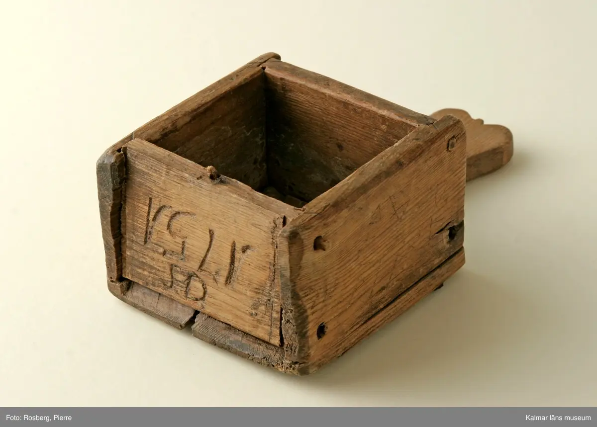 KLM 14360. Ostform. Av trä. Fyrkantig med botten utskjutande i form av ett handtag. Skuret mönster i botten, fyrkanter i varandra, minst i mitten och störst närmast kanten. Inskuren text: OS 1751.