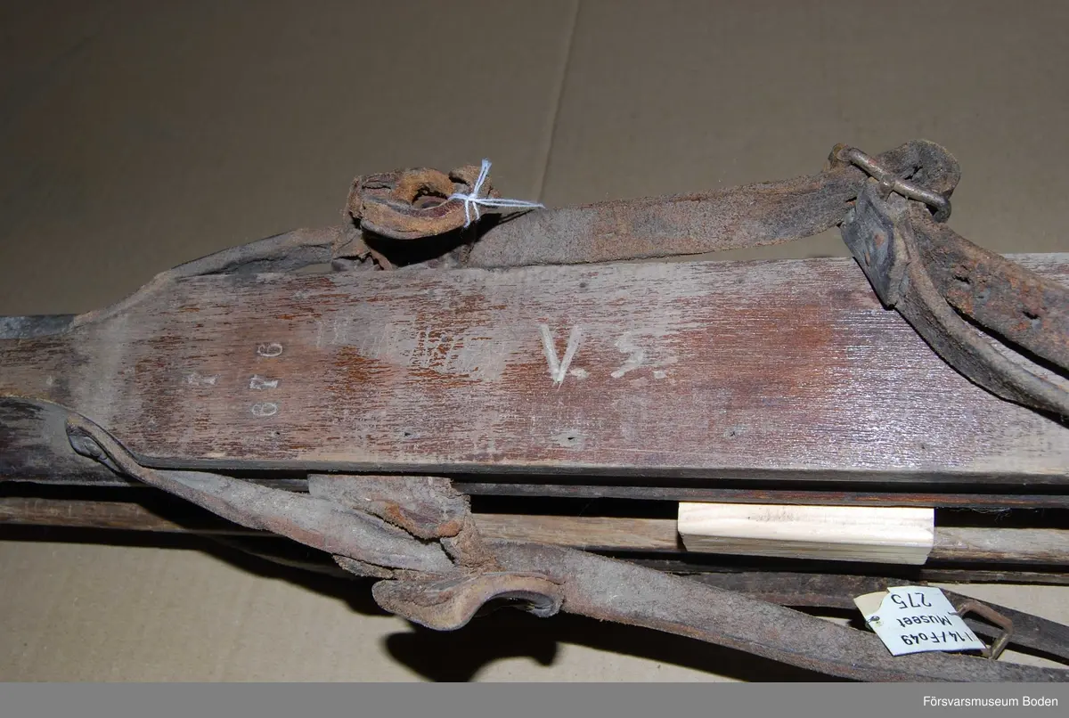 Mörkbruna skidor med låg spets och hög rygg liknande arméskidor m/1913. Fyrkantig profil på rännan undertill. Bindningar med remmar och sula av gummibelagd väv, varav den ena saknas. Den ena skidan har spruckit och reparerats med bleckplåt, men har fått en ny skada vid spetsen. Inga kronstämplar finns, däremot andra stämplar där den saknade sulan suttit. Till skidorna hör en etikett med texten "I 14/Fo 49 Museet 275".