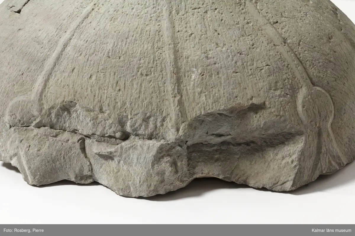 KLM 22431. Dopfunt, del av. Av kalksten, huggen. Botten av cuppan till godronnerad funt. Daterad till 1200-tal. Jfr. KLM 22766. Det finns vissa likheter.