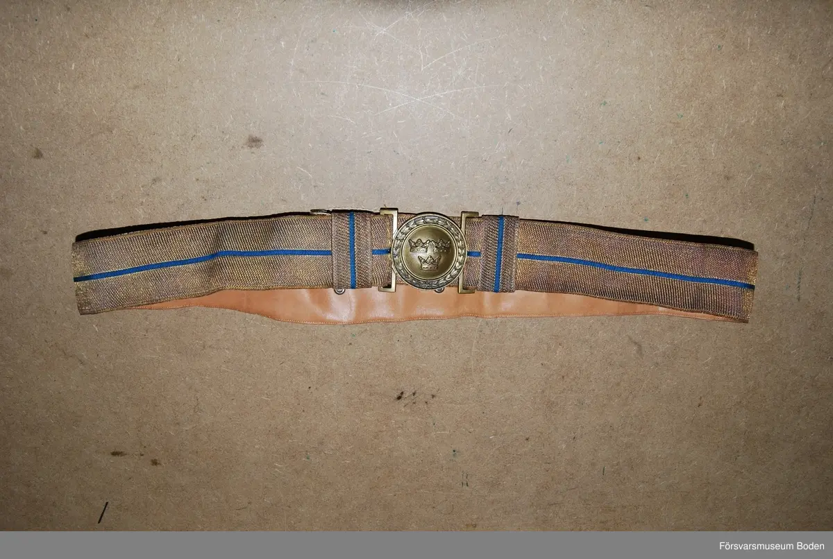 Bars till uniform m/1939 och m/1952 vid stor högtidsdräkt. Vävd av bronsfärgad tråd med smal blå rand inlagd. Spänne med tre kronor i brons, delat i två delar. För modellexemplar med utförlig beskrivning, se AM.004633.