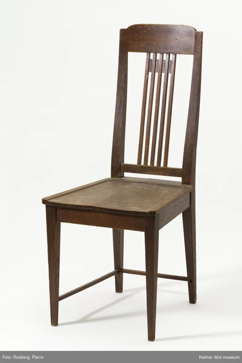 KLM 31932:1-2. Stol. 2 stycken. Av ek, träsits. Stolar med spjälrygg, ben med tunna bak- och sidoslåar. På båda stolarna är en sidoslå avbruten. Den ena stolens sits har en längsgående spricka. Stil: jugend.