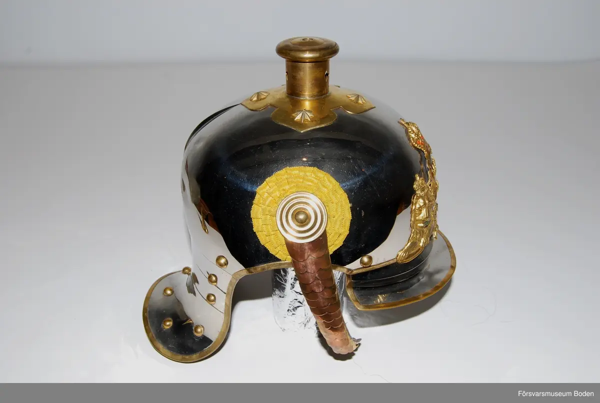 Förnicklad stålplåt med förgyllda beslag. Bl.a. förlängt nackstycke jämfört med tidigare m/1879. Upptill skruvfäste för plym m/1887 av vitt tagel (vid stor paraddräkt) eller pik, båda medföljer. Gul sidenkokard under hakremsknappen på höger sida. Framtill förgylld vapenplåt med blå emalj.