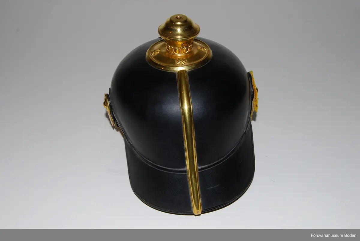 Svartlackerat läder med förgyllda beslag, framplåt, bakskena och hakrem. Förgyllt mössmärke med blå emalj. Gul sidenkokard under högra hakremsknappen. Med plym m/1885 av svart tagel, vilken användes vid stor paraddräkt. Pik medföljer ej.