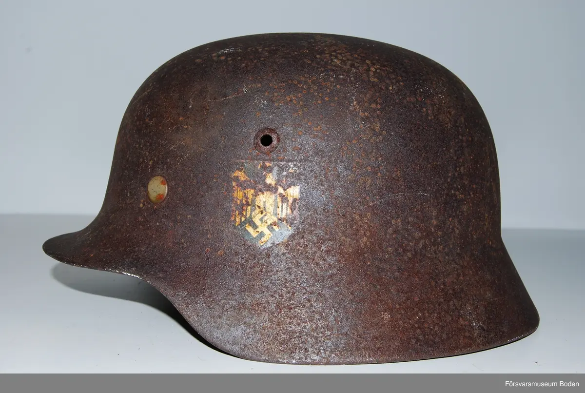 Kanten omvikt mot insidan. Inredning med aluminiumband, stämplat 1938. Rester av grön färg på insidan. Dekaler på båda sidor, varav endast rostkonturerna syns på den vänstra sidan. Storlek 59