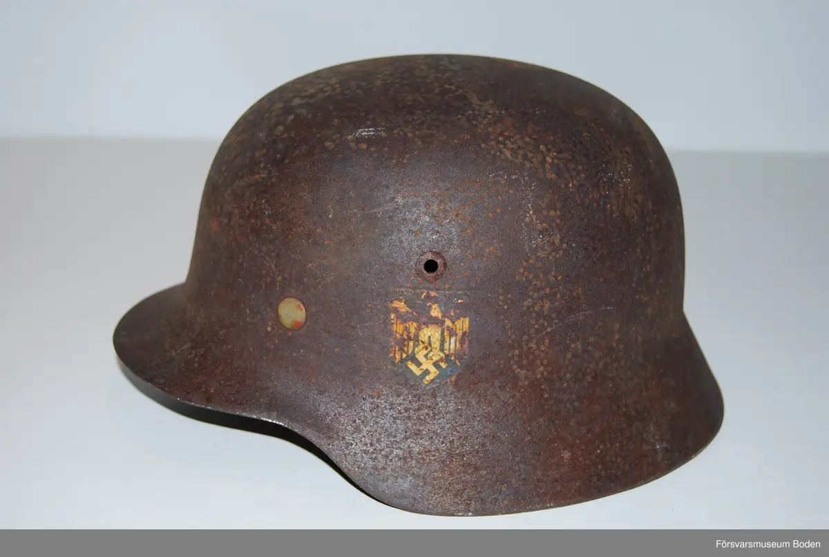 Kanten omvikt mot insidan. Inredning med aluminiumband, stämplat 1938. Rester av grön färg på insidan. Dekaler på båda sidor, varav endast rostkonturerna syns på den vänstra sidan. Storlek 59