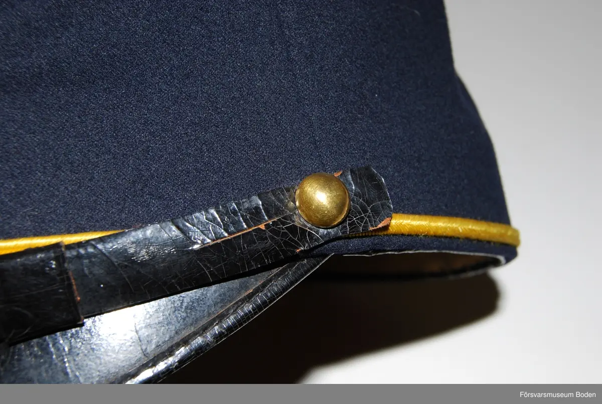 Mörkblått kläde med skärm och hakrem av svartlackerat läder. Hakremmen fastsatt på sidorna med kulknappar modell mindre för manskap. Gult beläggningssnöre runt mössans nedre del, format till ögla baktill. Framtill agraff bestående av kompanimärke m/1899 med siffran 5 av metall på gult kläde (nu blekt). Nertill kulknapp för manskap.