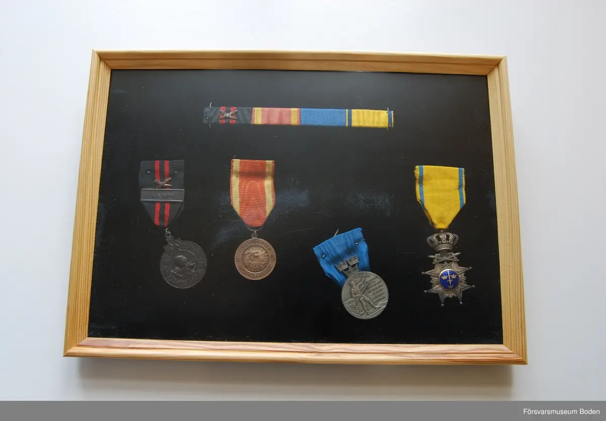 Tavla med uppsatta medaljer på svart sammet. Har tillhört Karl Hjalmar Lindskog, finlandsfrivillig 1939-1940. Från vänster på bilden:
1. Vinterkrigets minnesmedalj med svärd och spänne, Lappi, järn. Urkund finns i pärm under FMB.002361.
2. Frihetsmedaljen 2.klass, brons, urkund finns i pärm under FMB.002361.
3. Medalj från Föreningen för skolungdomens vapenövningar, silver.
4. Svärdstecken.
Överst på tavlan ett släpspänne för dessa medaljer.