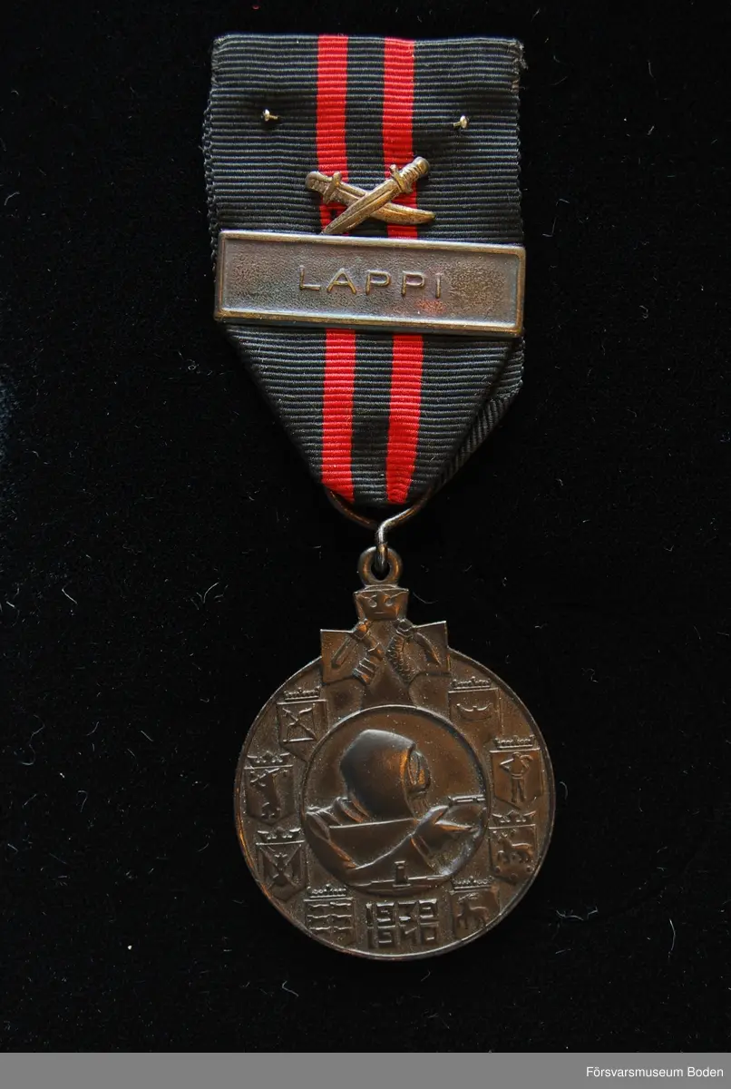 Tavla med uppsatta medaljer på svart sammet. Har tillhört Karl Hjalmar Lindskog, finlandsfrivillig 1939-1940. Från vänster på bilden:
1. Vinterkrigets minnesmedalj med svärd och spänne, Lappi, järn. Urkund finns i pärm under FMB.002361.
2. Frihetsmedaljen 2.klass, brons, urkund finns i pärm under FMB.002361.
3. Medalj från Föreningen för skolungdomens vapenövningar, silver.
4. Svärdstecken.
Överst på tavlan ett släpspänne för dessa medaljer.