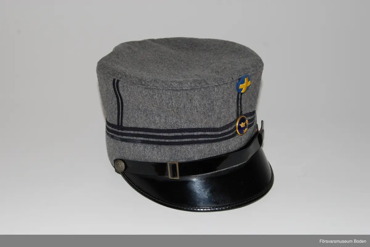 Ljusgrått kläde med tre smala band av blått kläde runt mössan betecknande kapten. Framtill mössmärke m/1865 i blå emalj samt upptill landstormsmärke m/1926 med gult broderat kors på blått kläde. Mössremmen fäst på sidorna med landstormens knapp modell mindre. Buren av fil. dr Arvid Moberg.