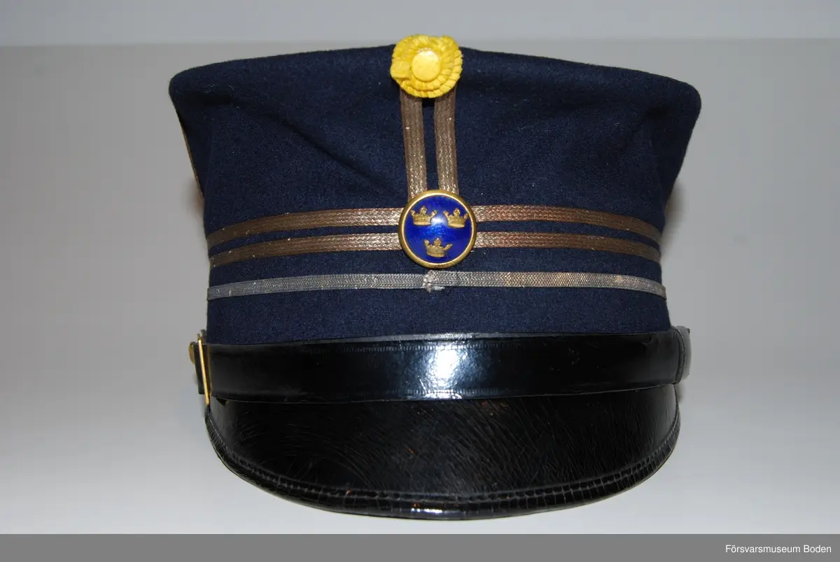 Mörkblått kläde med tre smala silvergaloner runt mössan betecknande kapten. Framtill mössmärke m/1865 med blå emalj för officererare, och ovanför detta gul sidenkokard. Mössremmen fäst på sidorna med artilleriets knapp modell mindre i guld. Buren av C.G. Dahlberg.