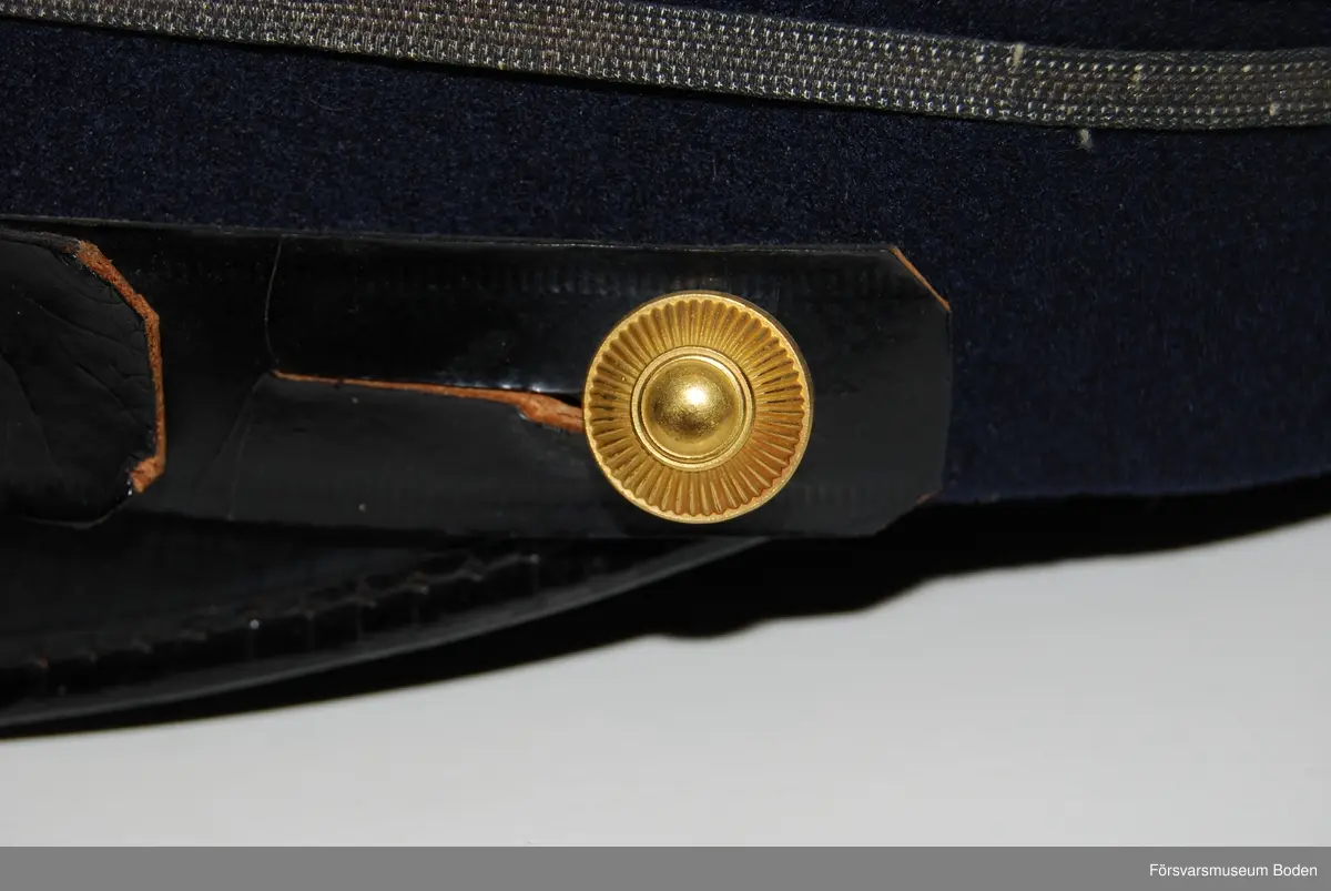 Mörkblått kläde med tre smala silvergaloner runt mössan betecknande kapten. Framtill mössmärke m/1865 med blå emalj för officererare, och ovanför detta gul sidenkokard. Mössremmen fäst på sidorna med artilleriets knapp modell mindre i guld. Buren av C.G. Dahlberg.
