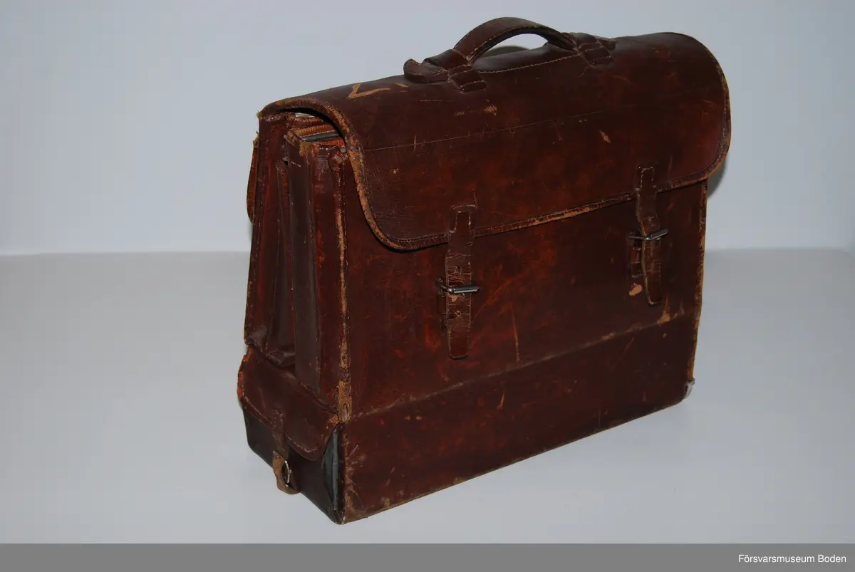 Utvikbar väska av brunt läder med låsbar låda av bleckplåt i botten, nyckeln saknas. Innehåller blanketter, kuvert, linjal m.m. (moderna utgåvor). Se AM.078470 för modellexemplar.
