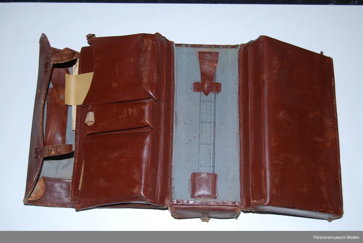 Utvikbar väska av brunt läder med låsbar låda av bleckplåt i botten, nyckeln saknas. Innehåller blanketter, kuvert, linjal m.m. (moderna utgåvor). Se AM.078470 för modellexemplar.