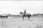 Skövde fältrittklubbs tävlingar 1932. Dressyrtävling på sandbanan öster om ridhuset. I bakgrunden järnpaddocken.