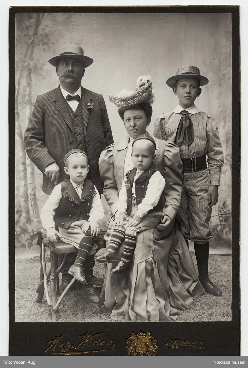 Familjeporträtt.Familjen Olners i Vimmerby.
Handlaren Emil Olners med hustrun Anna Maria f. Faleij och sönerna Einar, Arne och Bertil. De två yngsta iförda s.k. Nordmarksdräkter, folkdräkter från Norra Ny i Värmland.