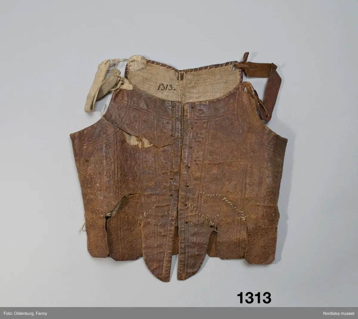 Katalogkort: "Lifstycke af brunt pressadt skinn. Öfver ryggsömmarna påsydda skinnremmar. Pressningen utgöres af ränder, våglinier, små rosetter m.m. Foder af hvit, grof linneväf. Å insidan af ena bröststycket märkt: "Segrin" med bläck. Till kvinnodräkt, enl. uppgift från 1700-talet."/P.G.Vistrand